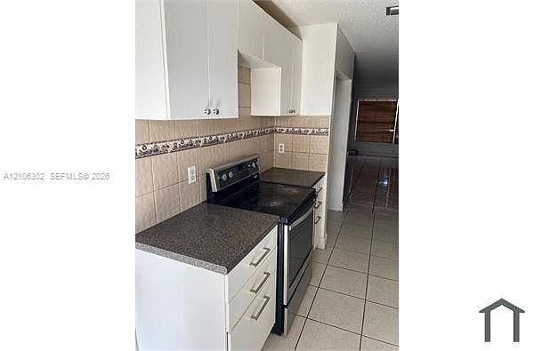 Kitchen featuring white cabinetry, dark countertops, a built-in black electric range, and tiled flooring