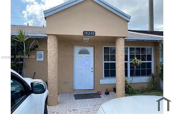 Exterior entryway featuring dual textured structural columns, a covered porch with patterned tile flooring, and multi-pane windows