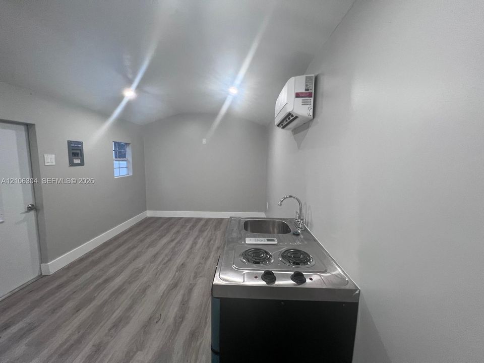 Interior space featuring wood-finish flooring, a wall-mounted ductless climate control unit, recessed ceiling lighting, and a stainless steel kitchenette unit with an integrated sink and two-burner cooktop