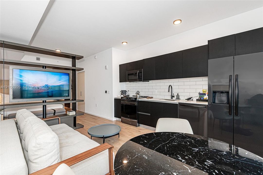 Kitchen featuring flat-panel dark cabinetry, white subway tile backsplash, stainless steel appliances, and wood-finish flooring