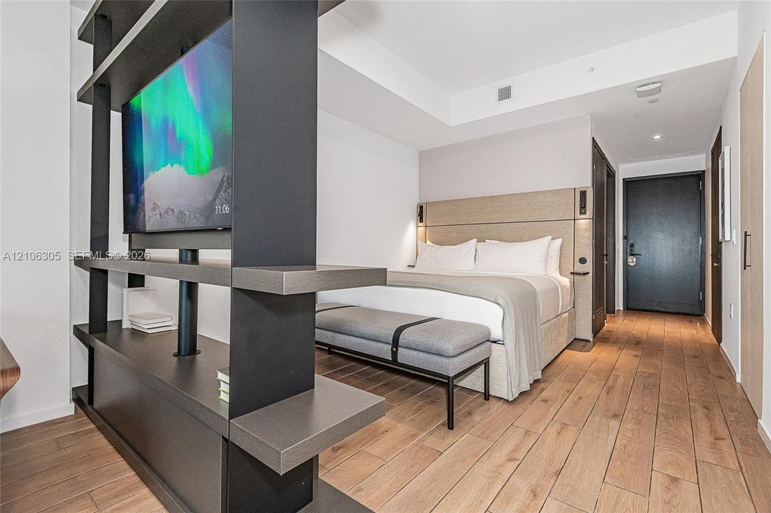 Wood-finish flooring, floor-to-ceiling built-in matte black shelving partition, and recessed ceiling lighting