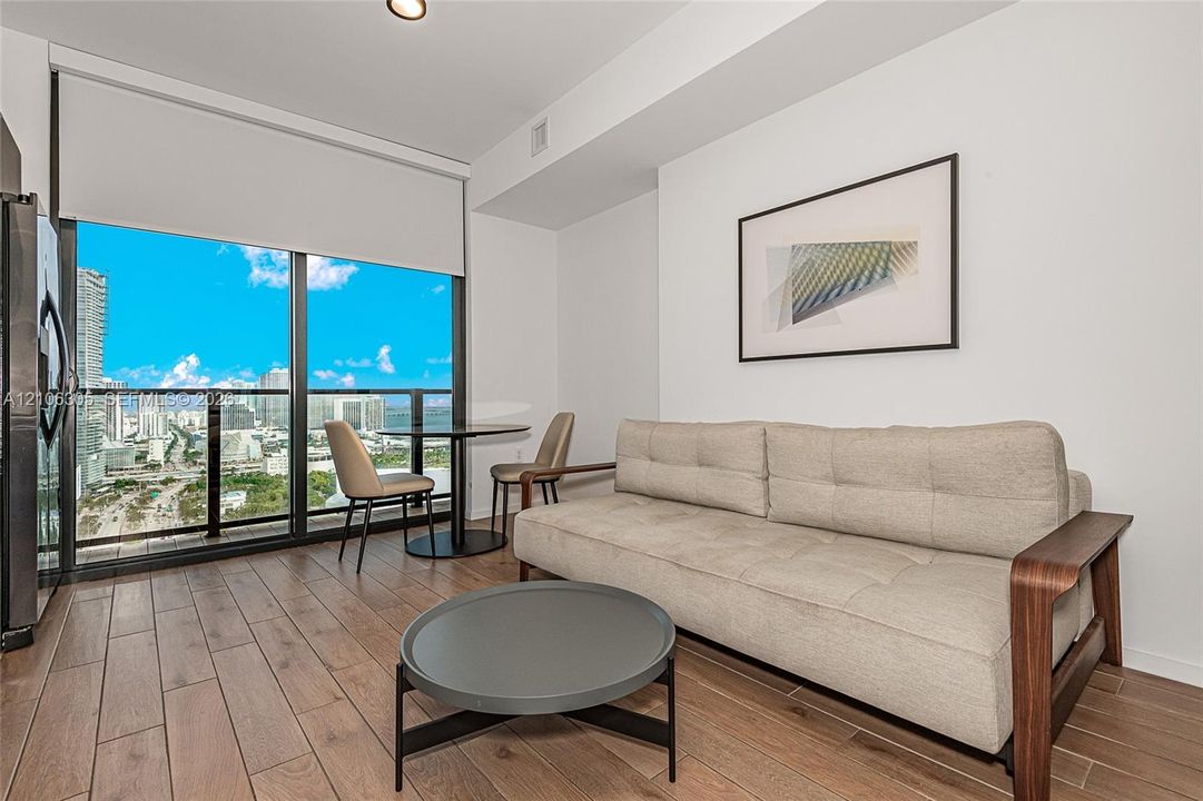 Floor-to-ceiling windows featuring automated roller shades, wood-finish tile flooring, and a private balcony with glass railing