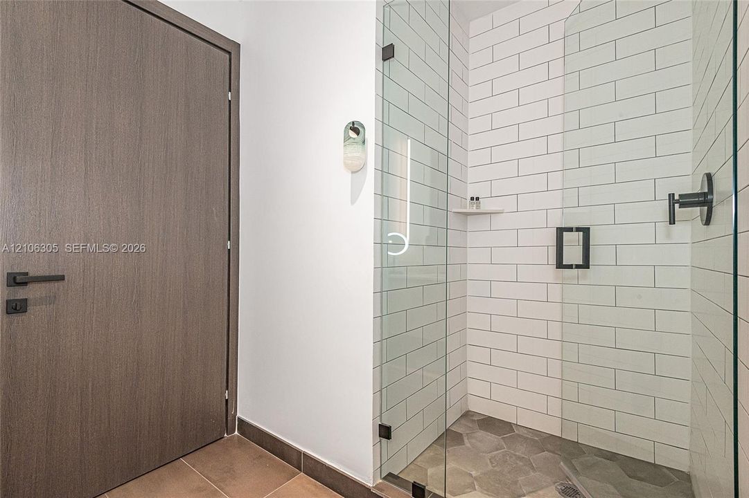 Walk-in shower featuring white subway tile walls, hexagonal floor tile, frameless glass enclosure, and matte black hardware