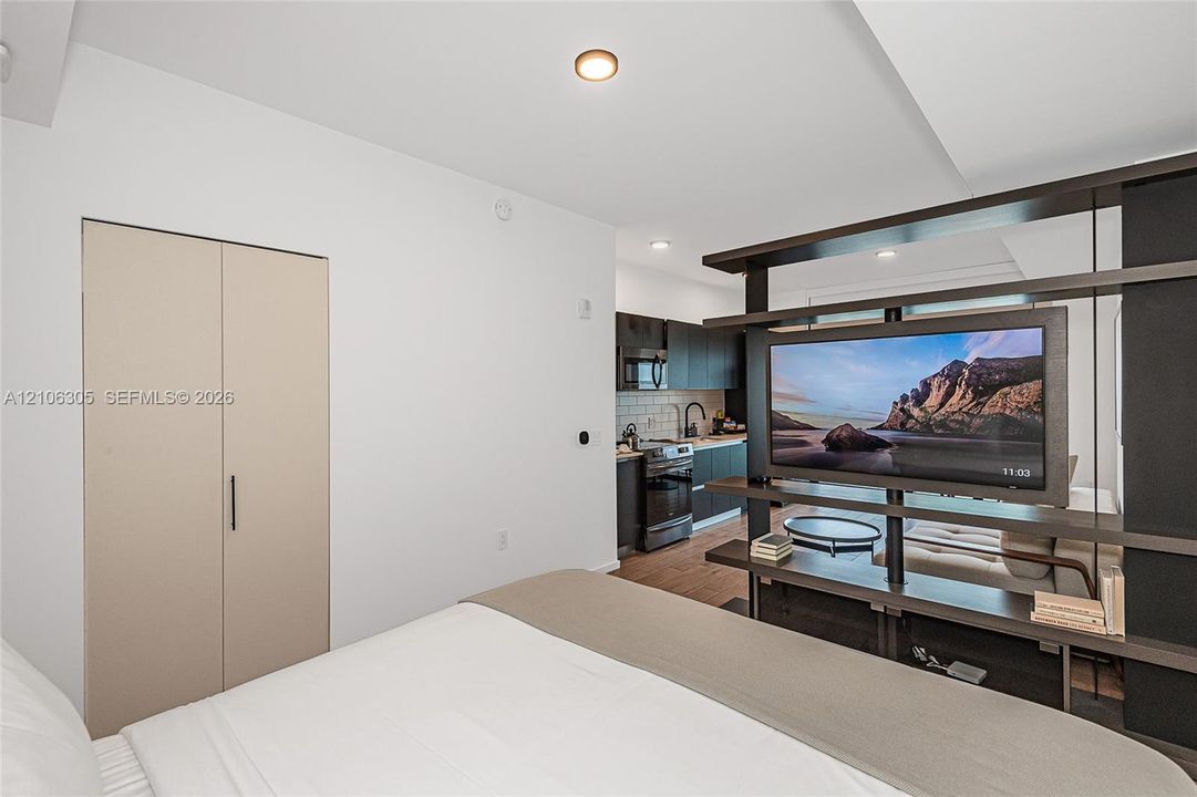 Built-in shelving unit, cabinetry with dark matte finish, white subway tile backsplash, and closet with flat-panel doors