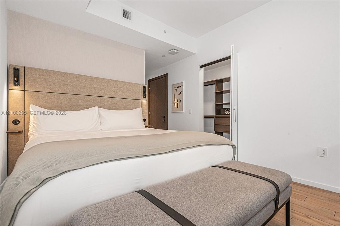 Built-in fabric headboard with integrated lighting, wood-finish flooring, and customized walk-in closet shelving