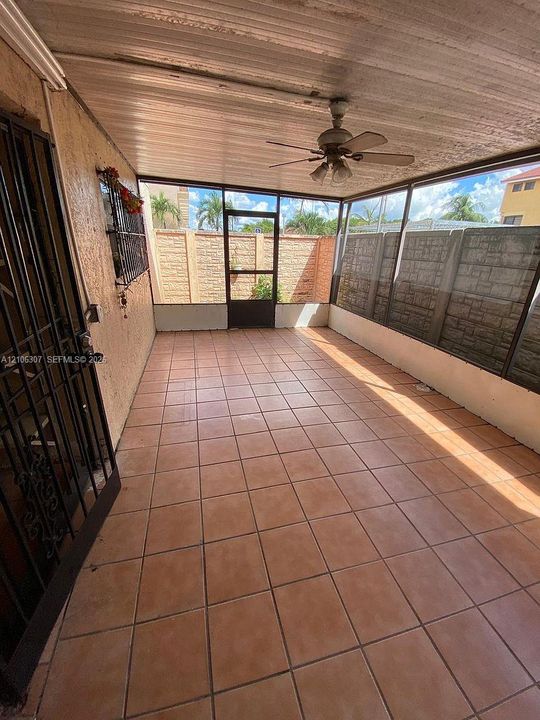 Screened-in patio featuring tile flooring, a corrugated metal ceiling, a central ceiling fan, and decorative masonry perimeter walls