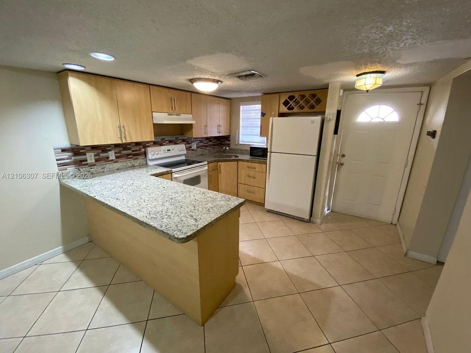 Kitchen featuring light-finish cabinetry, stone-texture countertops, mosaic tile backsplash, tile flooring, and integrated wine storage