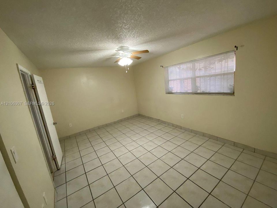Neutral-toned room featuring large-format ceramic tile flooring, a centered ceiling fan with integrated light fixture, and a single window with horizontal blinds