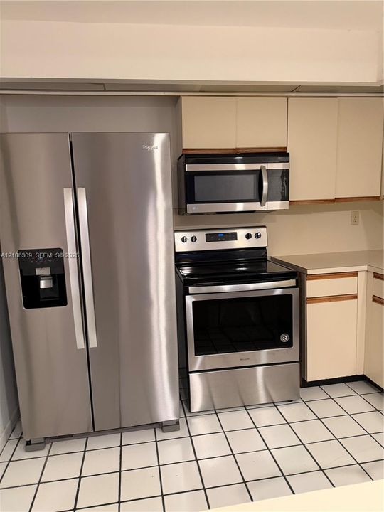 Stainless steel side-by-side refrigerator, stainless steel electric range, built-in microwave, light-toned cabinetry, and tiled flooring