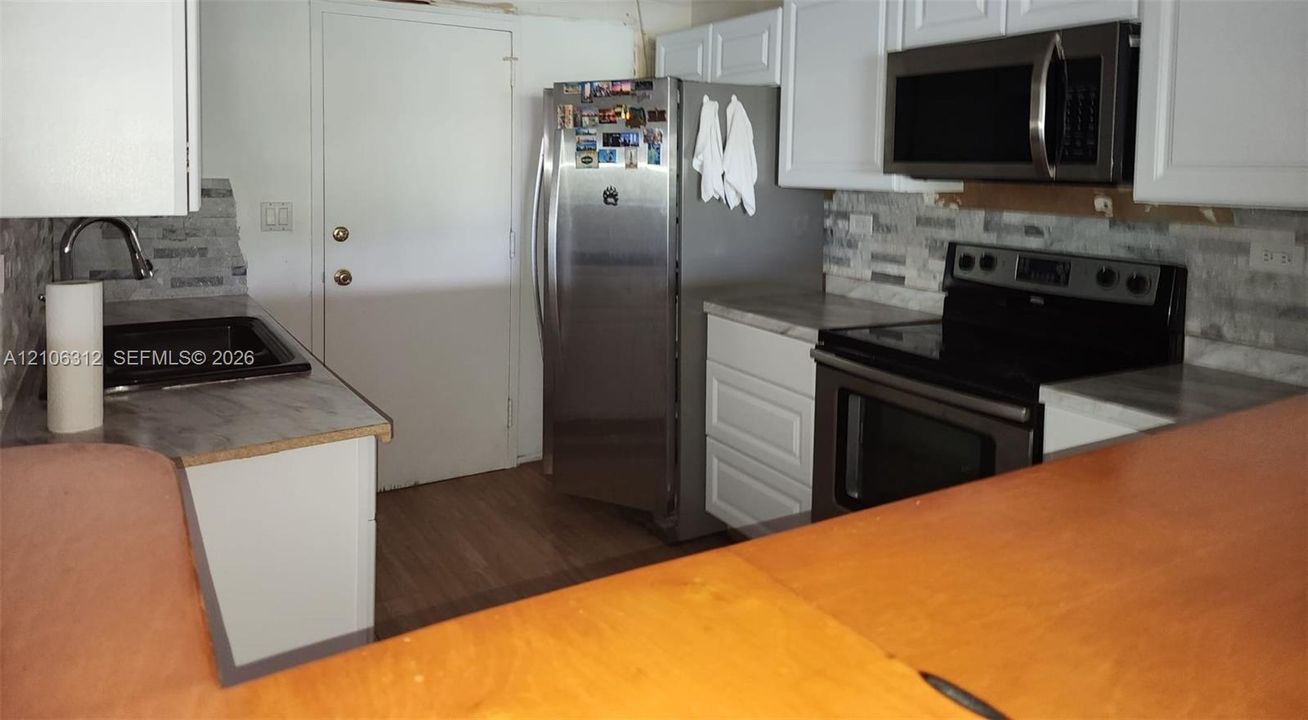 Kitchen featuring white cabinetry, stainless steel appliances, neutral stone-tile backsplash, and solid-surface countertops