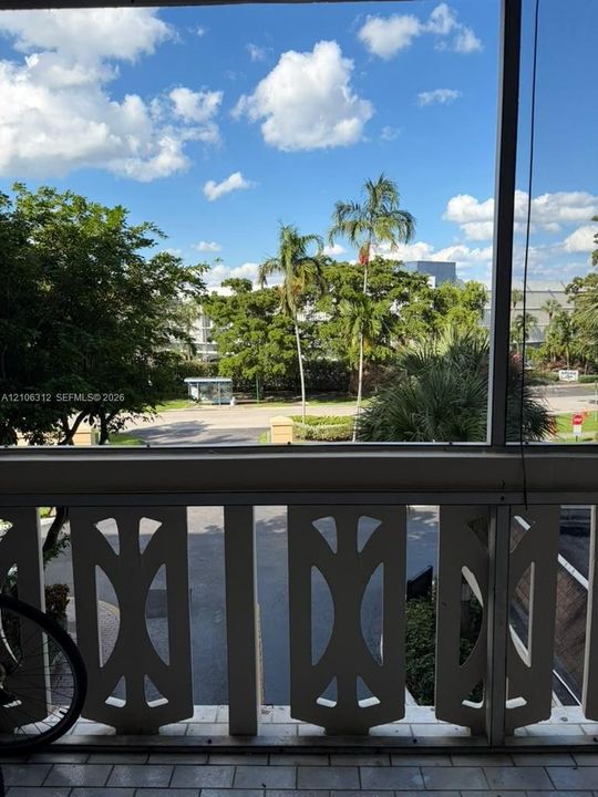 Screened balcony featuring decorative white geometric railing and tiled flooring, overlooking mature palm trees and green space