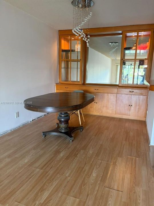 Built-in wooden cabinetry featuring glass-front display sections, a central mirror, and integrated storage, accented by a contemporary spiral crystal chandelier and wood-finish flooring