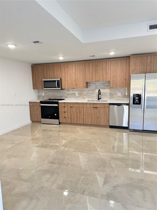 Kitchen featuring flat-panel wood cabinetry, light stone-finish countertops, stainless steel appliances, a matte black faucet, and large-format tile flooring