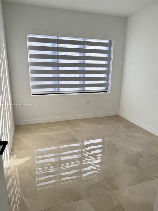 Room featuring polished large-format tile flooring, neutral wall finishes, and a window equipped with horizontal zebra-style blinds