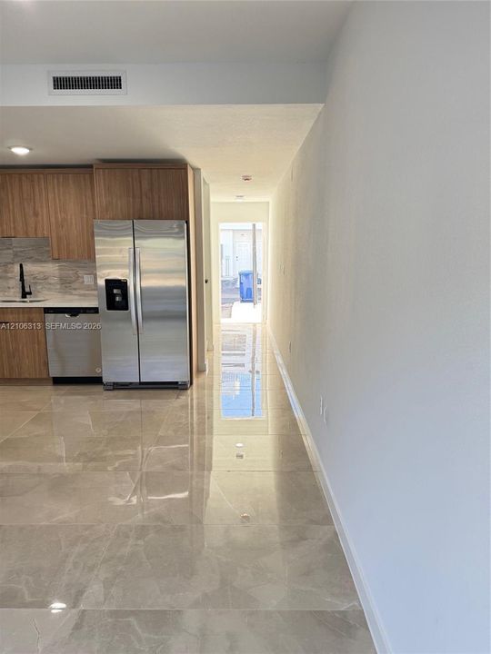 Kitchen area featuring light wood-finish cabinetry, stainless steel appliances, a stone-finish tile floor, and a stone-finish backsplash