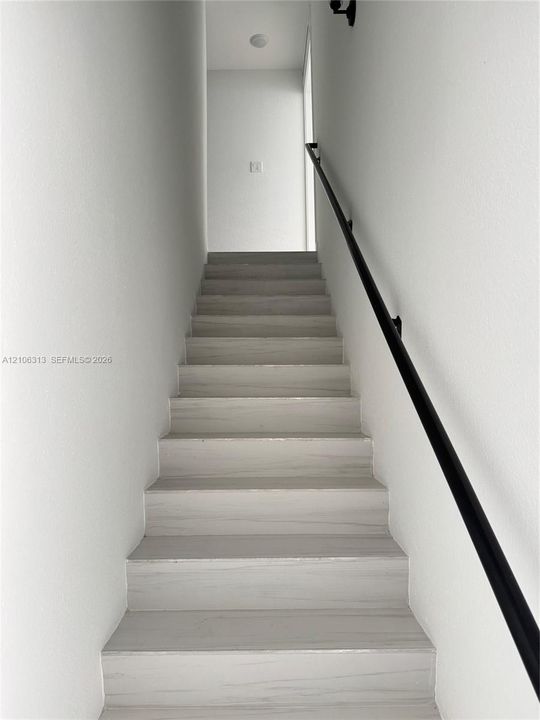 Staircase featuring wood-finish treads and a matte black wall-mounted handrail