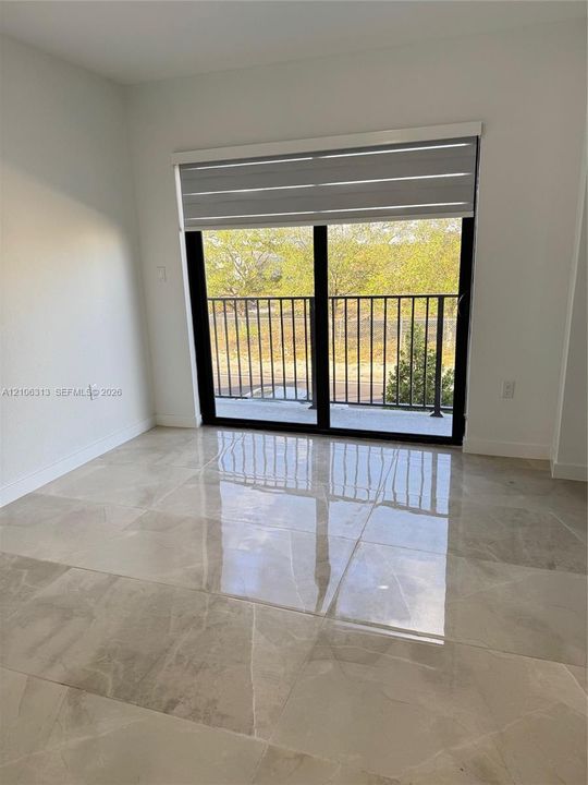 Large-format tile flooring, sliding glass door with black frame, retractable window shade, and exterior balcony featuring metal railing