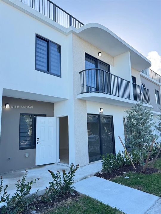 Contemporary two-story exterior featuring smooth stucco siding, a curved architectural roofline, metal balcony railings, and a rooftop terrace