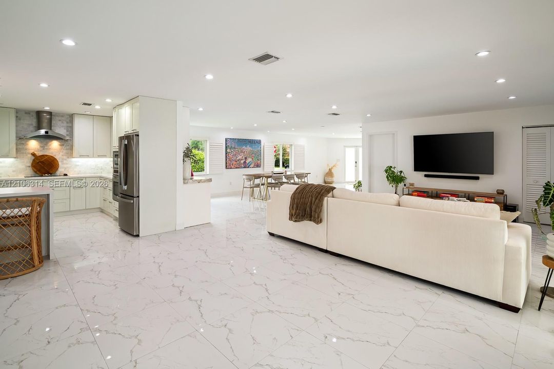 Open-concept interior featuring large-format veined tile flooring, recessed ceiling lighting, flat-panel cabinetry, and stainless steel kitchen appliances