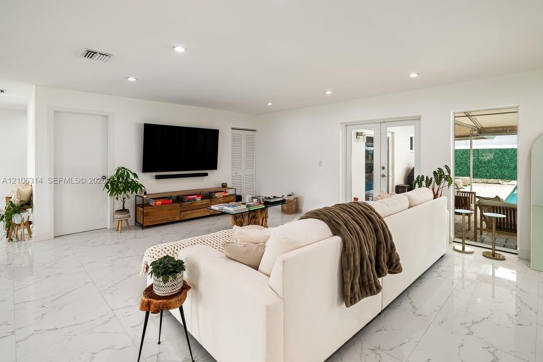 Interior living space featuring polished, large-format stone-look porcelain tile flooring, recessed lighting, and glass-paned double doors leading to the exterior
