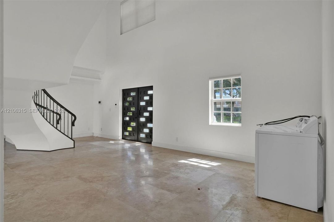 Double-height foyer featuring stone tile flooring, a curved staircase with a metal handrail, and a decorative double entry door with glass paneling