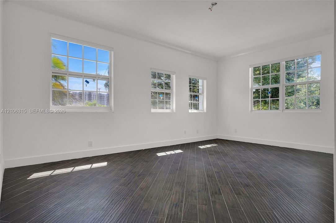 Interior space featuring dark wood-finish flooring, white walls, and multiple multi-pane windows with grid detailing