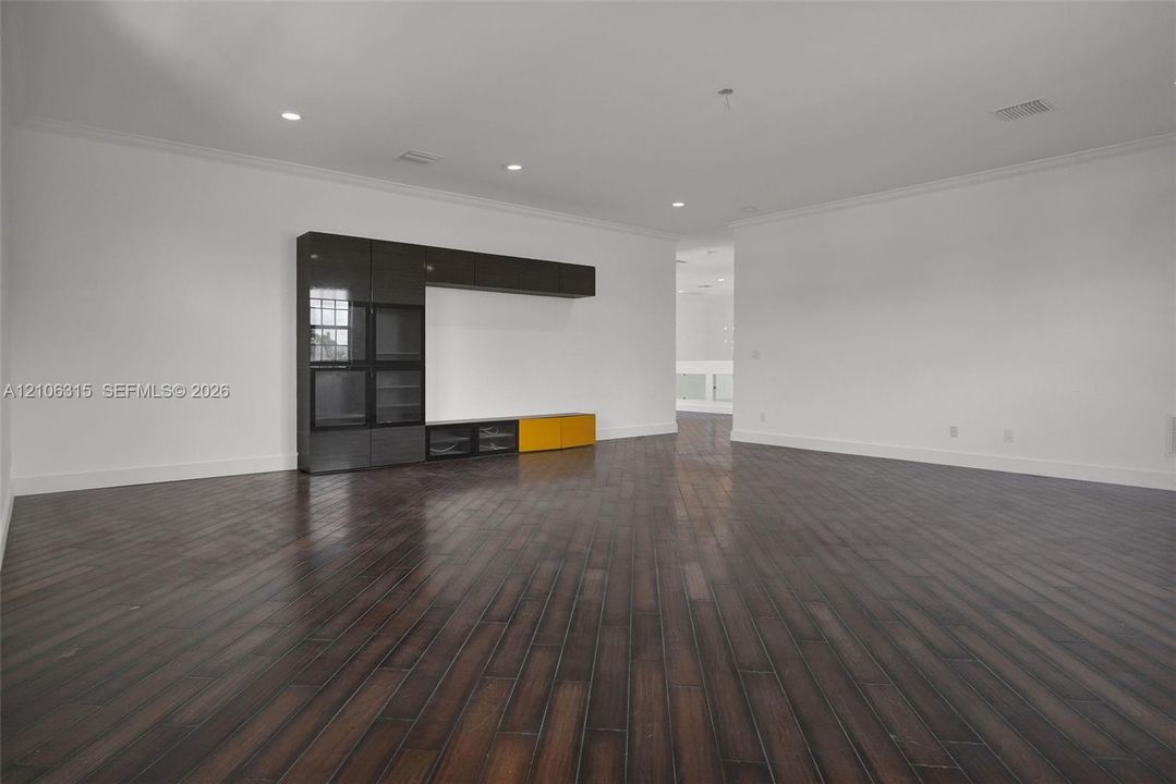 Spacious interior featuring dark wood-finish flooring, recessed lighting, crown molding, and built-in cabinetry with glass-front storage