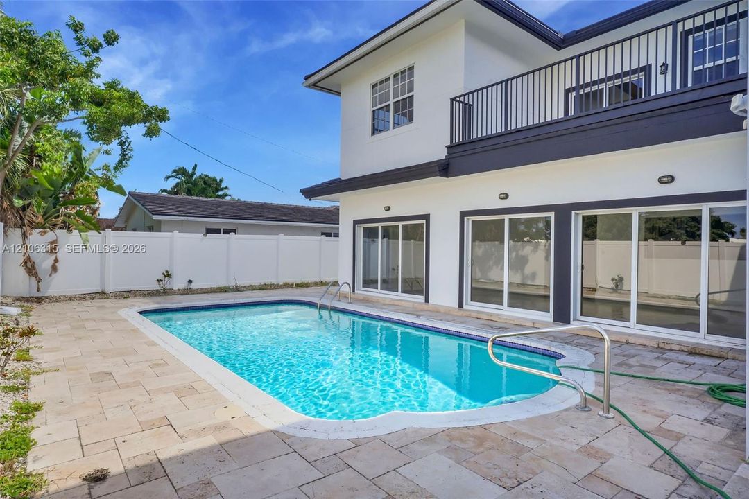 Exterior featuring a white stucco facade, private swimming pool, stone paver decking, white vinyl perimeter fencing, and an upper-level balcony with metal railing