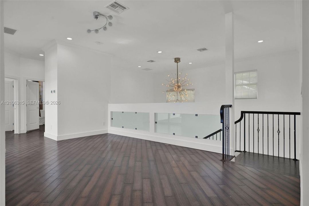 Wood-finish flooring, matte black metal railings, frosted glass safety panels, starburst-style chandelier, and recessed lighting