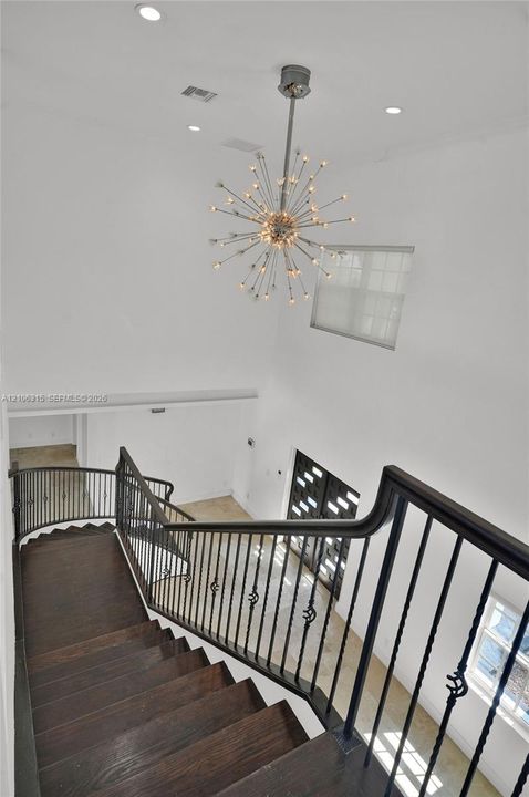 Staircase featuring dark wood-finish treads and a decorative metal railing, highlighted by a multi-point sputnik-style chandelier, recessed lighting, and high-ceiling architecture