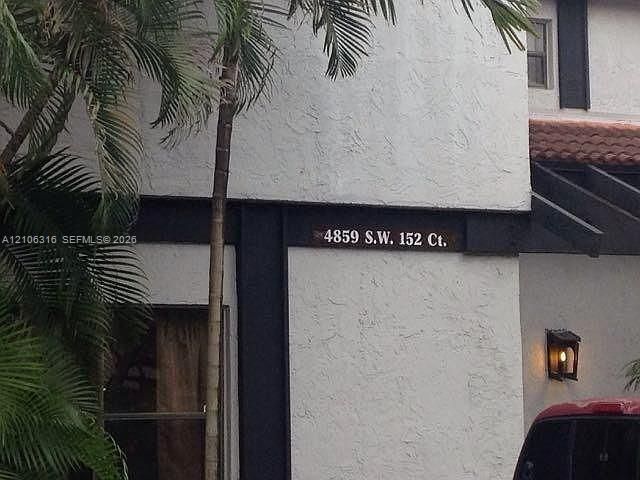 Textured stucco exterior featuring dark wood-finish structural accents, a tiled roof line, and a wall-mounted outdoor light fixture