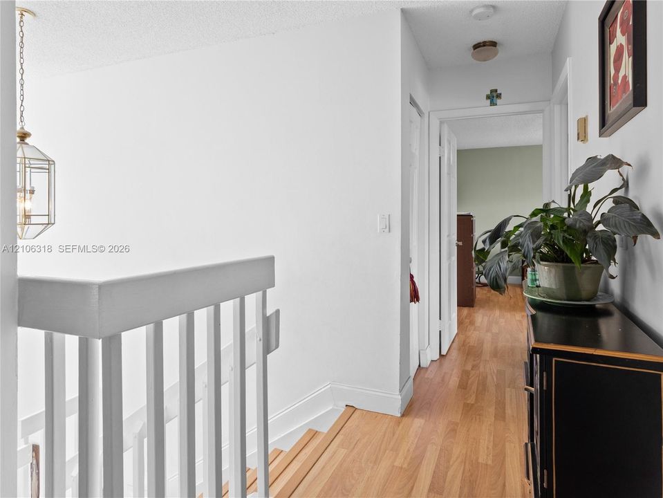 Hallway featuring wood-finish flooring, white staircase railing, and a geometric pendant light fixture