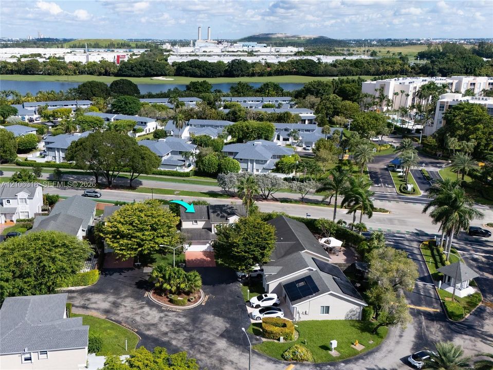 Aerial perspective of a multi-story residence featuring a shingled roof, attached garage, and paved driveway situated within a landscaped community