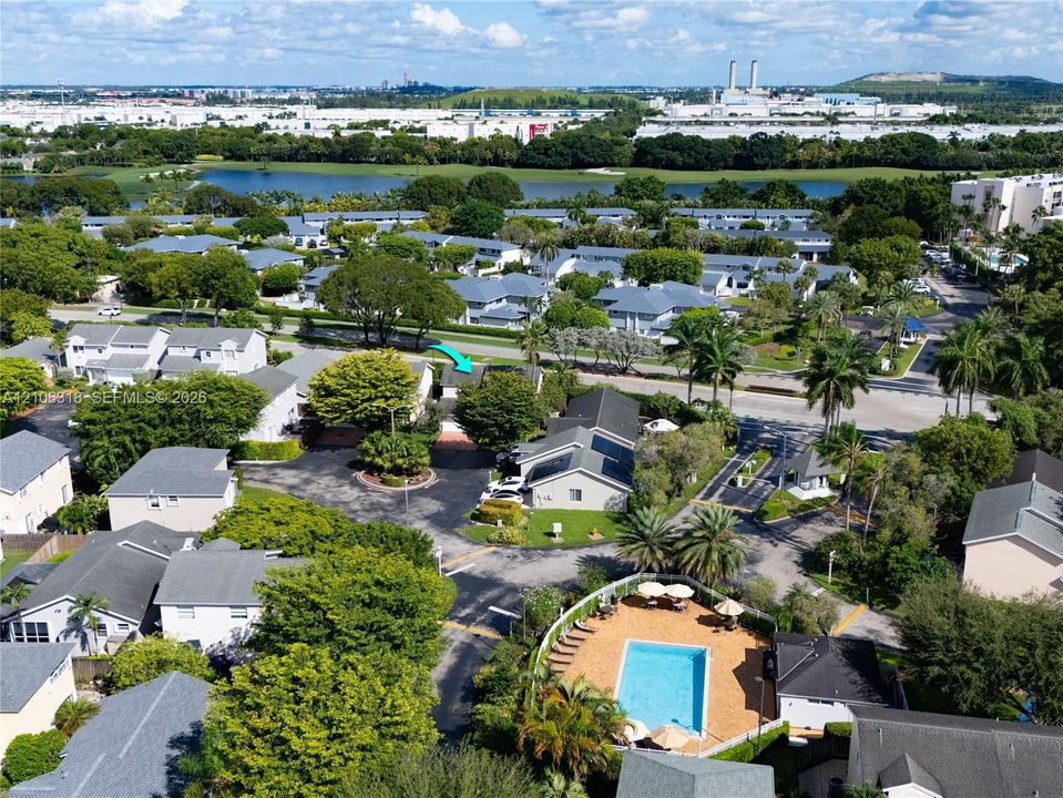 Aerial perspective featuring a residential community with mature landscaping, a swimming pool, and water features