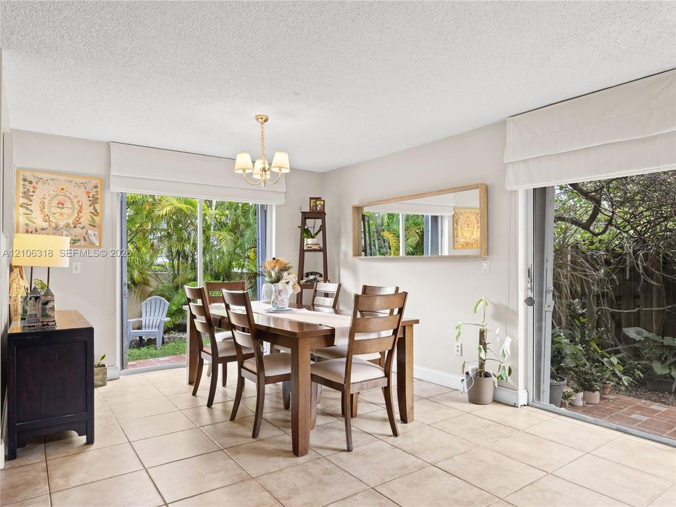 Dining space featuring large-format tile flooring, dual sliding glass doors, a decorative chandelier, and a wall-mounted rectangular mirror