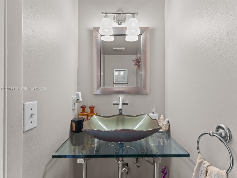Floating glass vanity with a scalloped basin, chrome single-handle faucet, wall-mounted mirror with a metallic frame, and a dual-light fixture