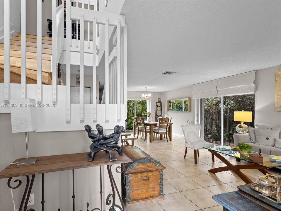 Open-concept interior featuring large-format tile flooring, a staircase with white vertical balusters and wood treads, and sliding glass doors
