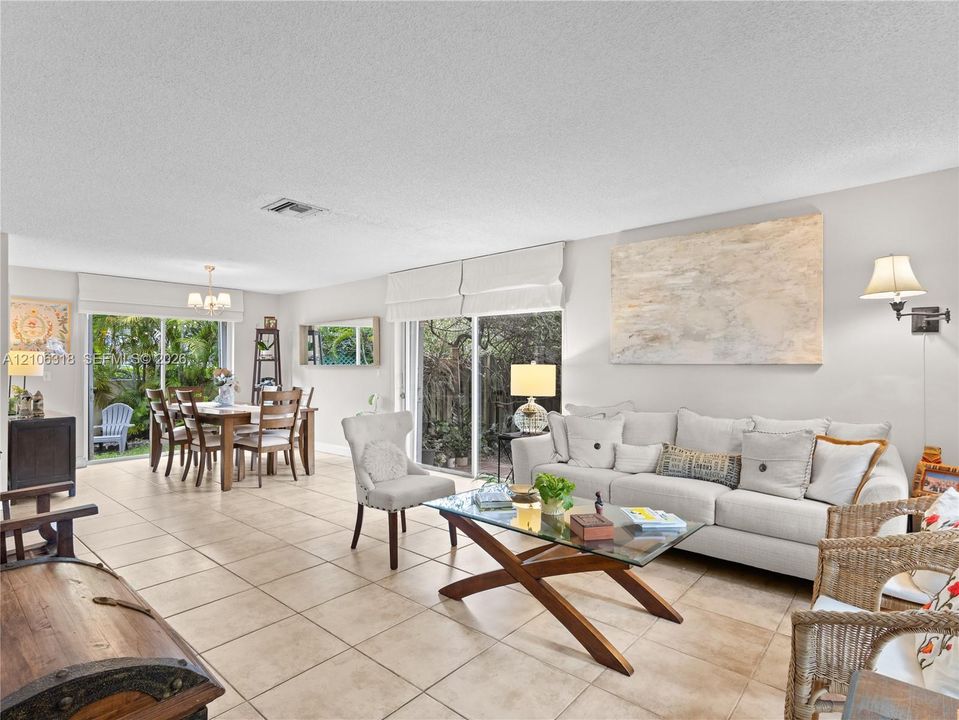 Open-concept living space featuring neutral ceramic tile flooring, dual sliding glass doors, and wall-mounted light fixtures
