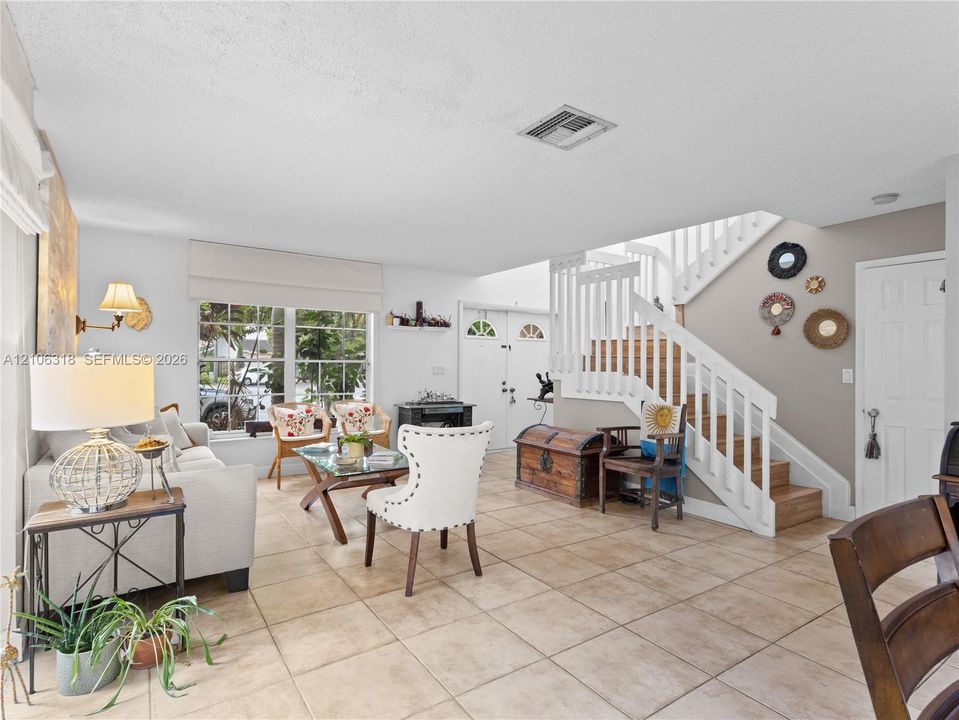 Open-concept living space featuring large-format tile flooring, a multi-pane window with Roman shades