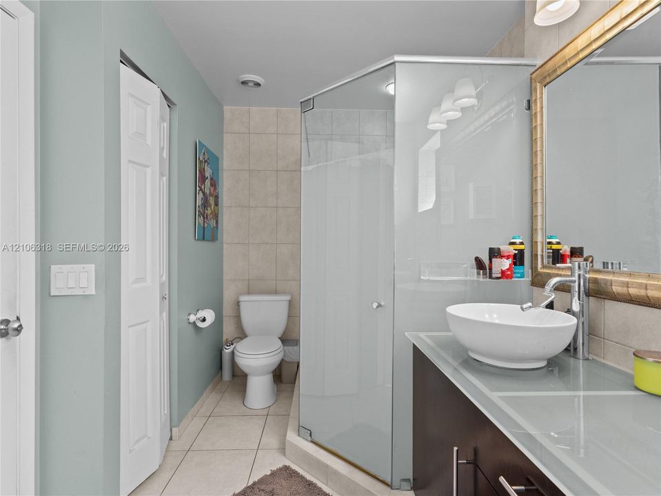 Vanity featuring a glass countertop and oval vessel sink, framed wall mirror, corner glass-enclosed shower, and tile flooring