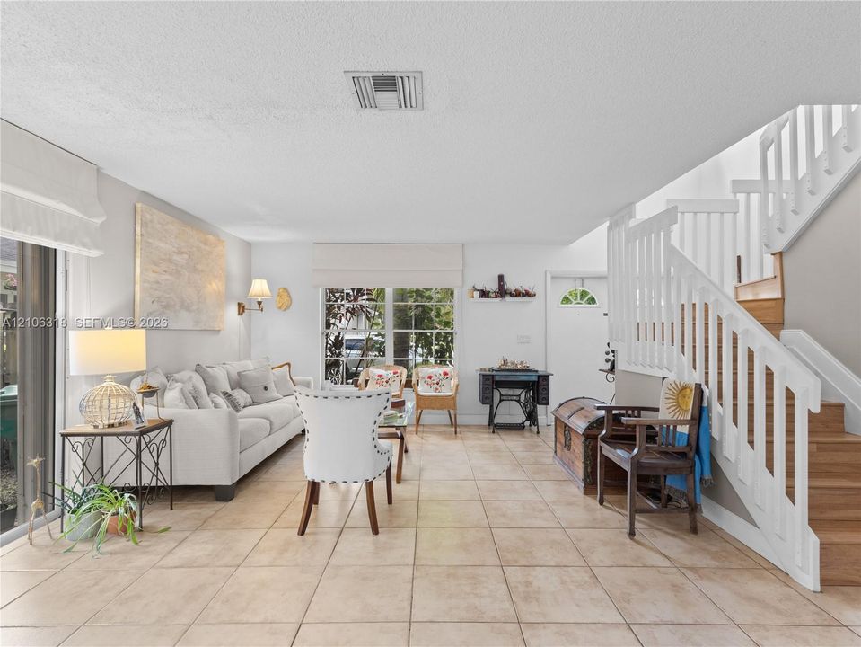 Open-concept space featuring tile flooring, staircase with white wooden balusters, and large glass sliding doors