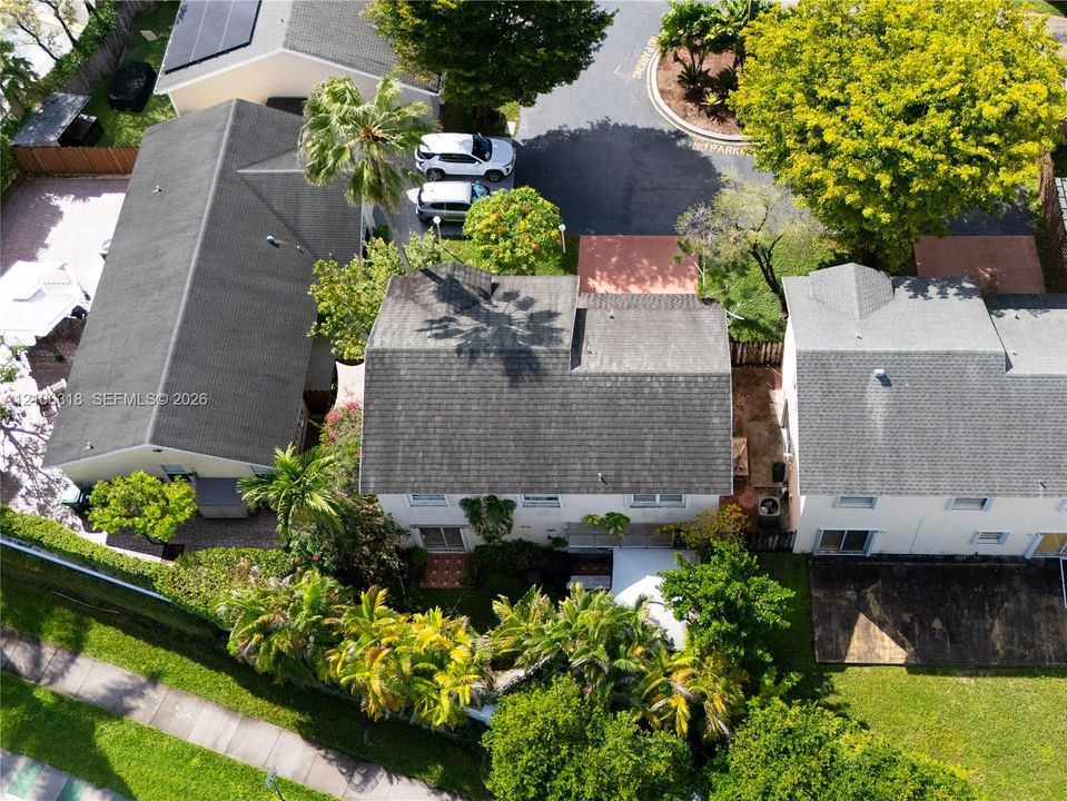 Aerial perspective featuring a multi-story residence with a shingled roof, attached garage, private rear patio area, and mature landscaping