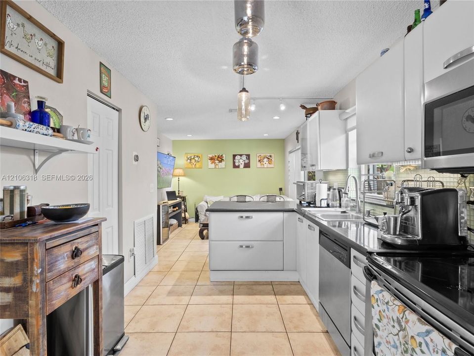 Kitchen featuring white cabinetry, solid-surface countertops, tile flooring, recessed lighting, and a stainless steel dishwasher