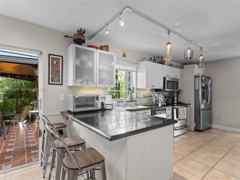 Kitchen featuring white cabinetry with glass-panel upper doors, dark stone-finish countertops, stainless steel appliances, and adjustable track lighting