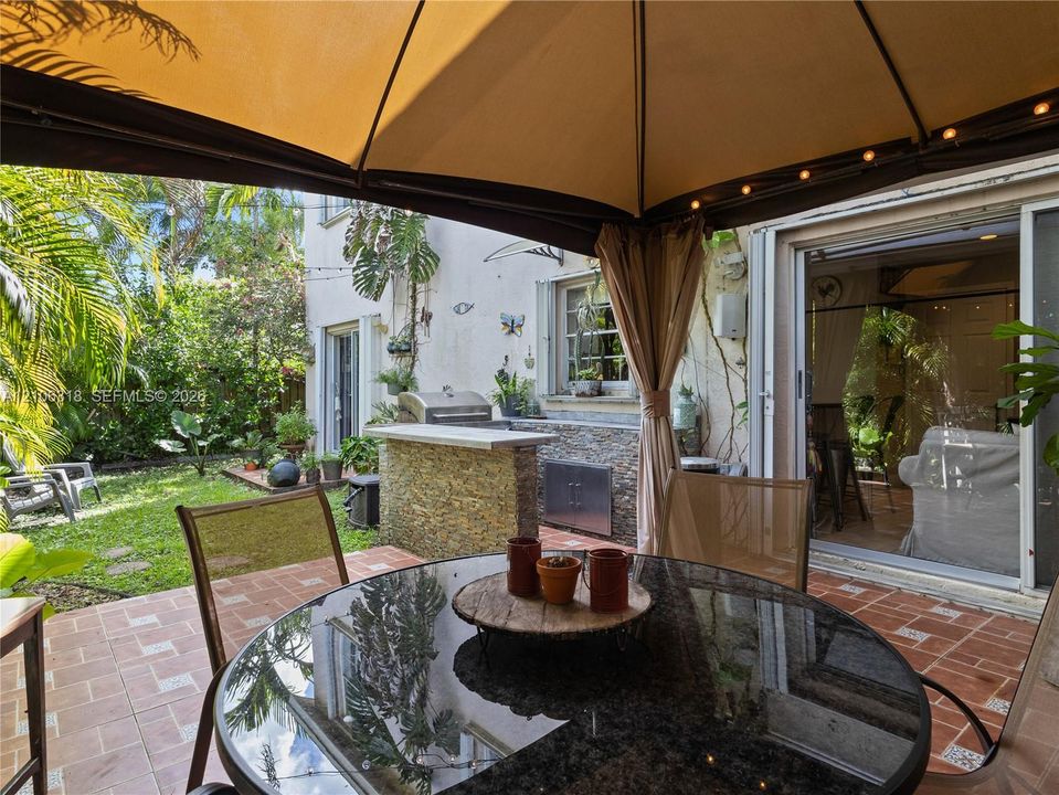 Outdoor living space featuring a built-in outdoor kitchen with stone veneer, stainless steel grill, tile patio flooring, and a permanent gazebo structure