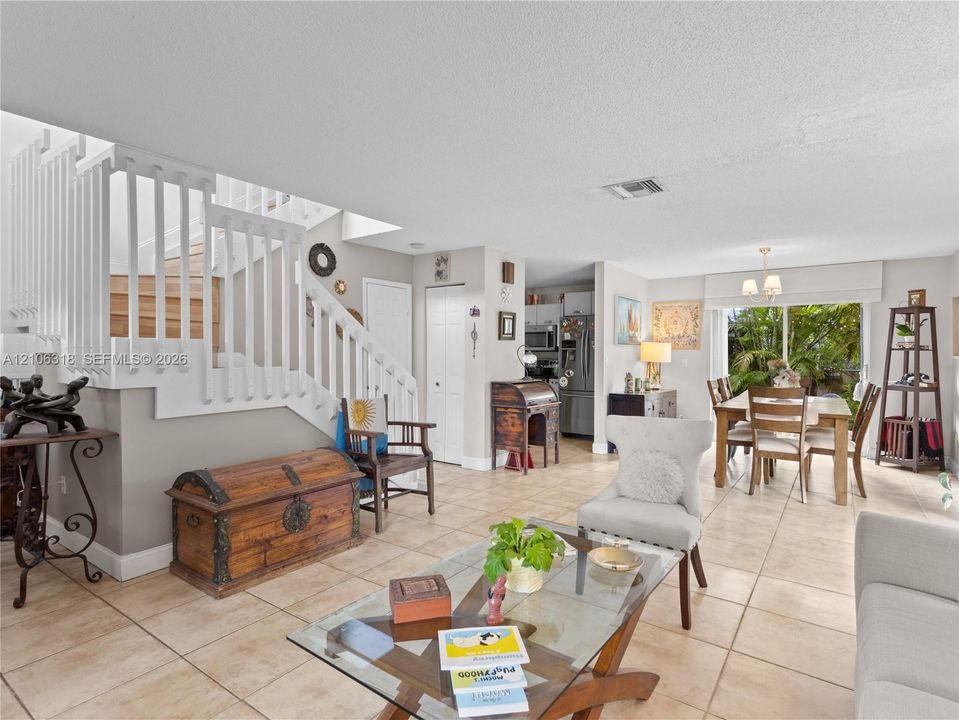 Open-concept interior featuring large-format tile flooring, a staircase with white balusters, and sliding glass doors with exterior access