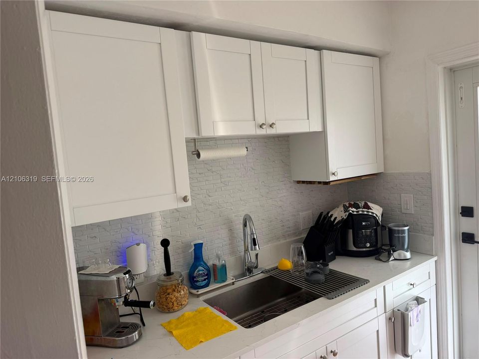 White shaker-style cabinetry, light-toned countertop, undermount stainless steel sink, pull-down chrome faucet, and textured tile backsplash