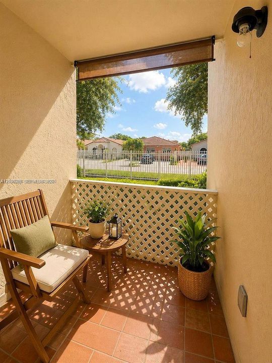 Covered terrace featuring terra-cotta tile flooring, white diamond-pattern lattice railing, and a retractable sun shade