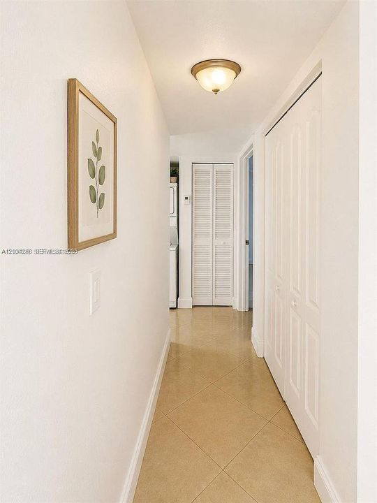 Hallway featuring neutral-toned tile flooring, white bi-fold closet doors, and a flush-mount ceiling light fixture