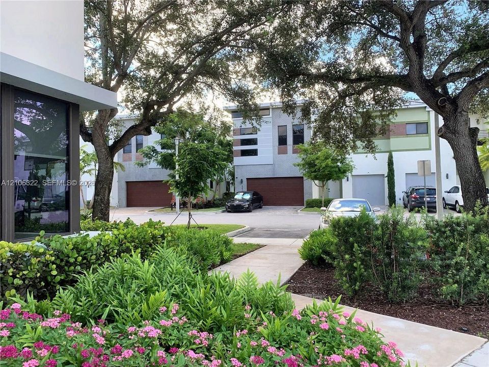 Contemporary multi-story exteriors featuring stucco facades, horizontal windows, attached garages with sectional doors, and mature shade trees complemented by manicured landscaping with paved walkways
